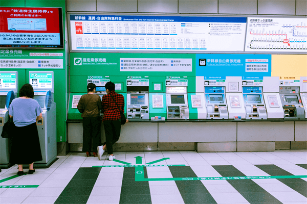 People using automated ticket kiosk machines at a train station equipped with thermal printer mechanisms
